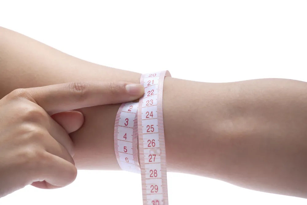 Close-up of woman measuring her arm with measurement tape.